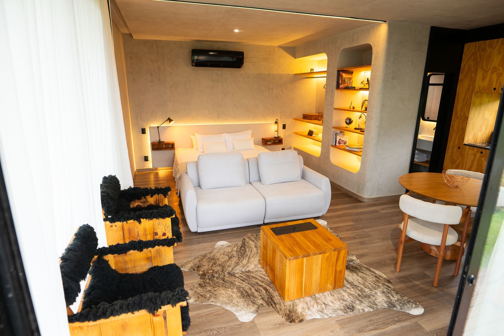 Sala de estar moderna com sofá branco, mesa de centro de madeira, cadeiras pretas e iluminação embutida aconchegante.