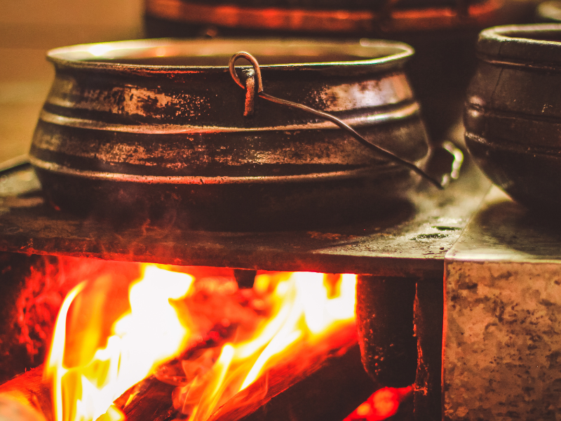 Panela pendurada sobre uma fogueira, com as chamas aquecendo-a em um ambiente rústico de cozinha.