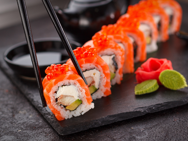 Rolinhos de sushi em um prato de ardósia preta com pauzinhos e wasabi, decorados com ovas vermelhas.
