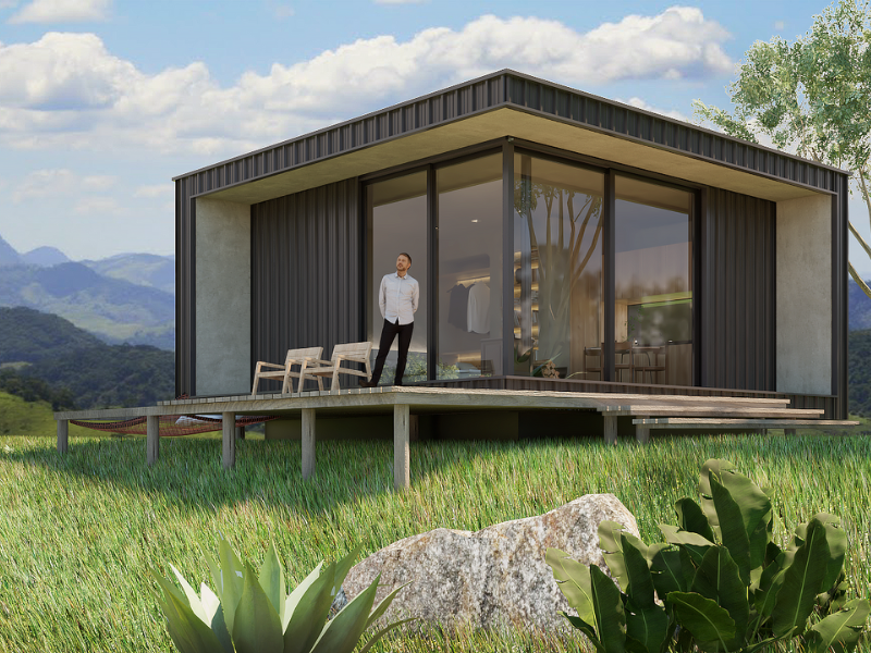 Cabana moderna em uma encosta gramada com uma pessoa em pé no deck e montanhas ao fundo.