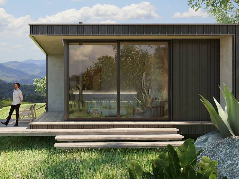 Cabana moderna com fachada de vidro, deck, degraus e exuberante vegetação ao redor, com uma pessoa em pé nas proximidades.