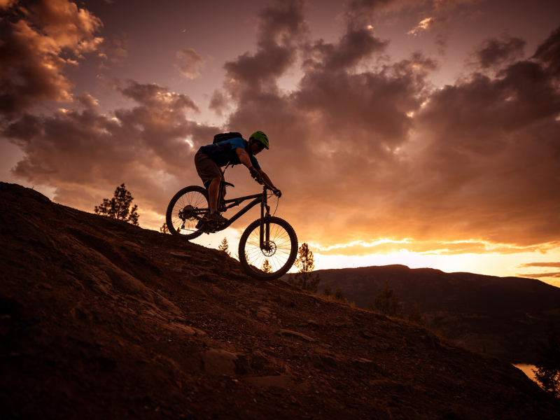 Silhueta de um ciclista de montanha em uma crista ao pôr do sol sob nuvens dramáticas.
