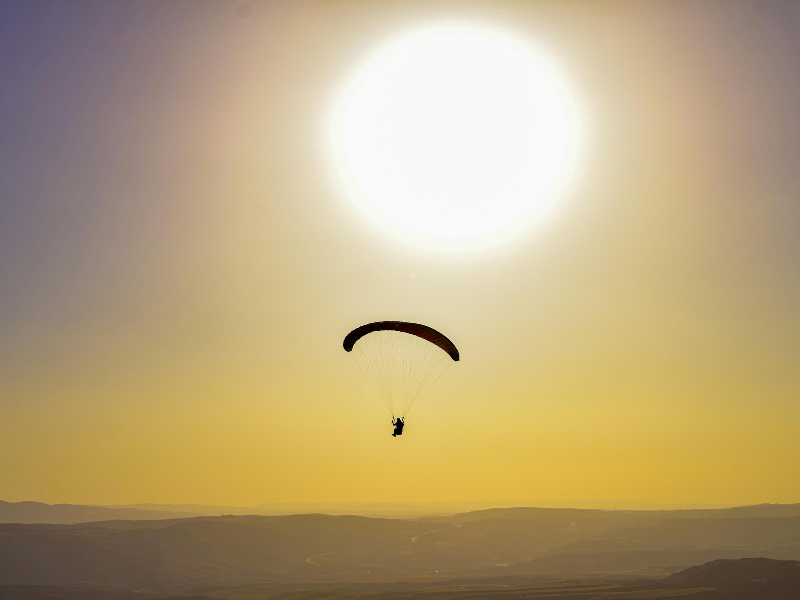 Silhueta de parapente contra um pôr do sol brilhante sobre colinas enevoadas.