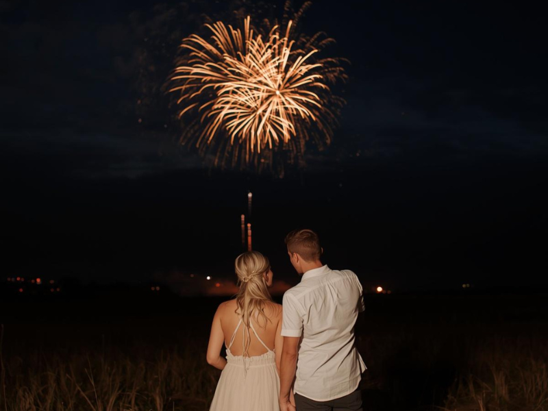 Casal assistindo a fogos de artifício dourados sobre um campo escuro à noite.