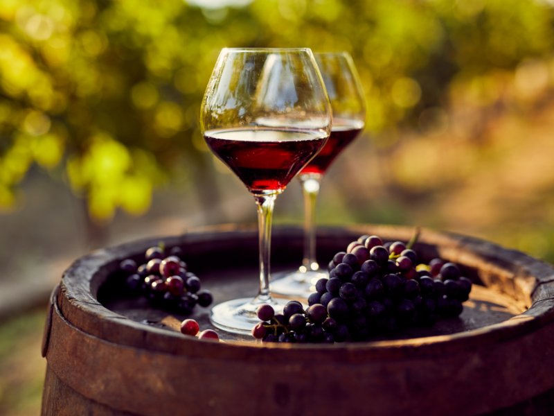 Taça de vinho com vinho tinto e frutos silvestres sobre um barril rústico ao ar livre