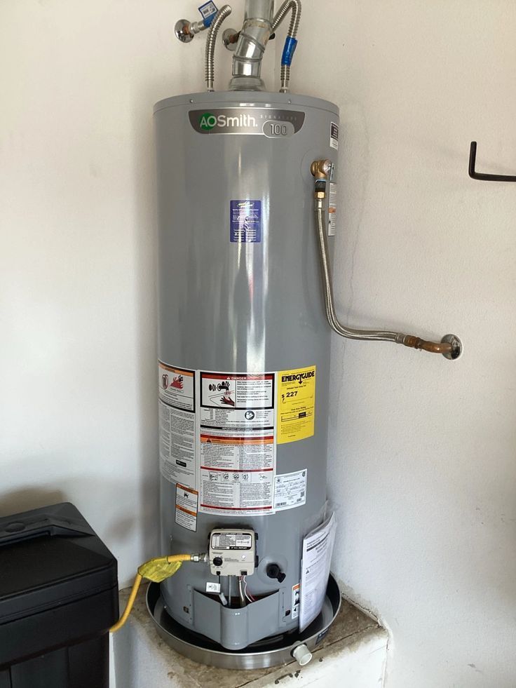 A grey A.O. Smith gas water heater sits in a drain pan on a raised platform in a garage.
