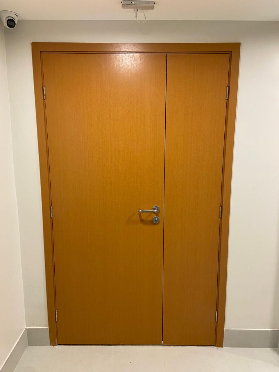 Uma grande porta de madeira está aberta em um corredor.