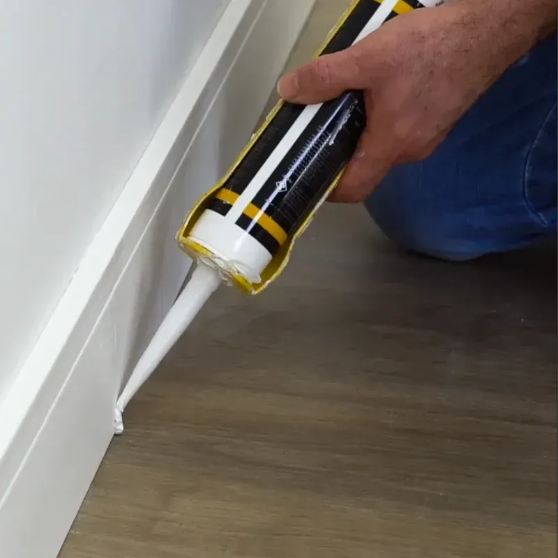 Uma pessoa está aplicando calafetagem em um piso de madeira