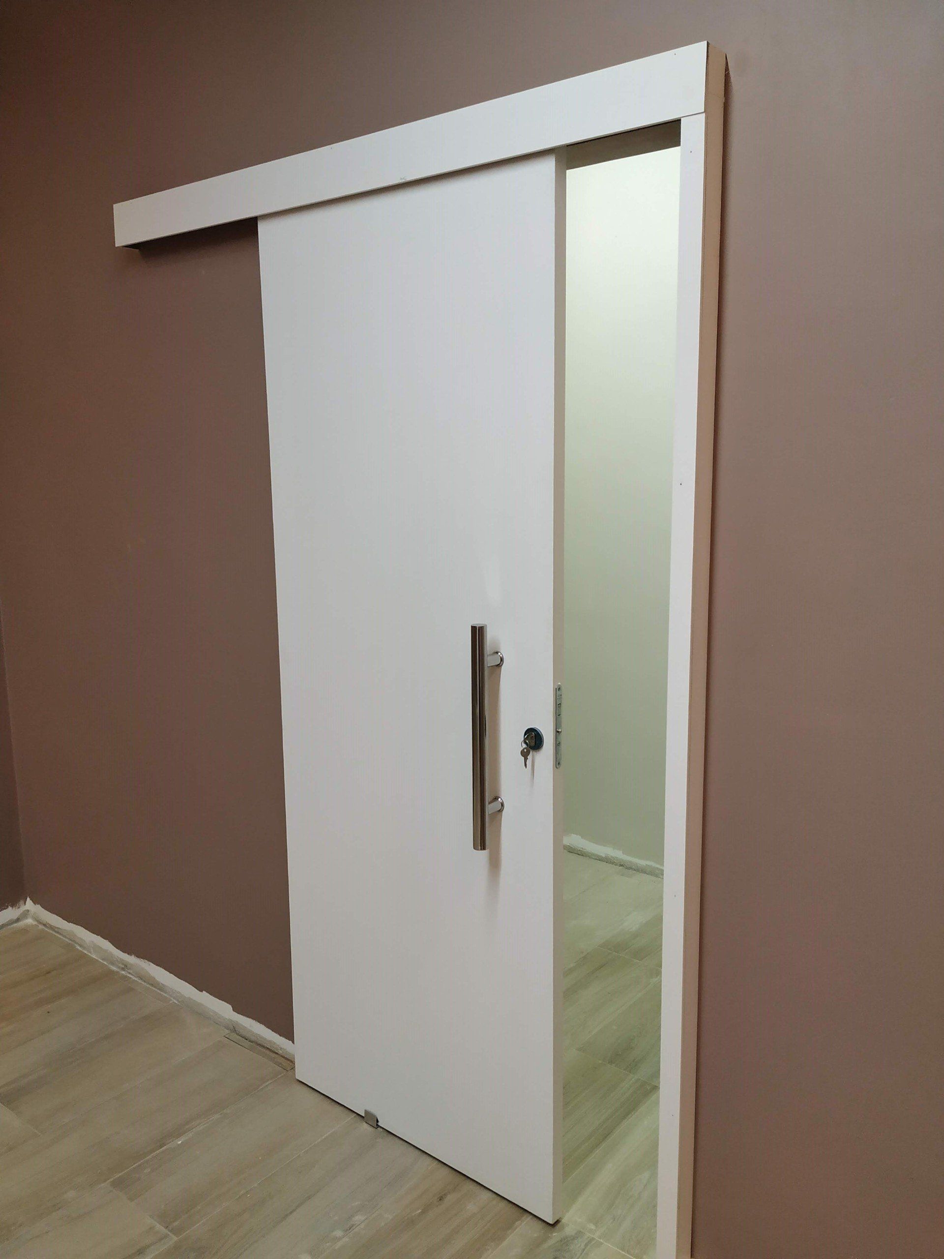 Uma porta de correr branca está aberta em uma sala com paredes marrons.