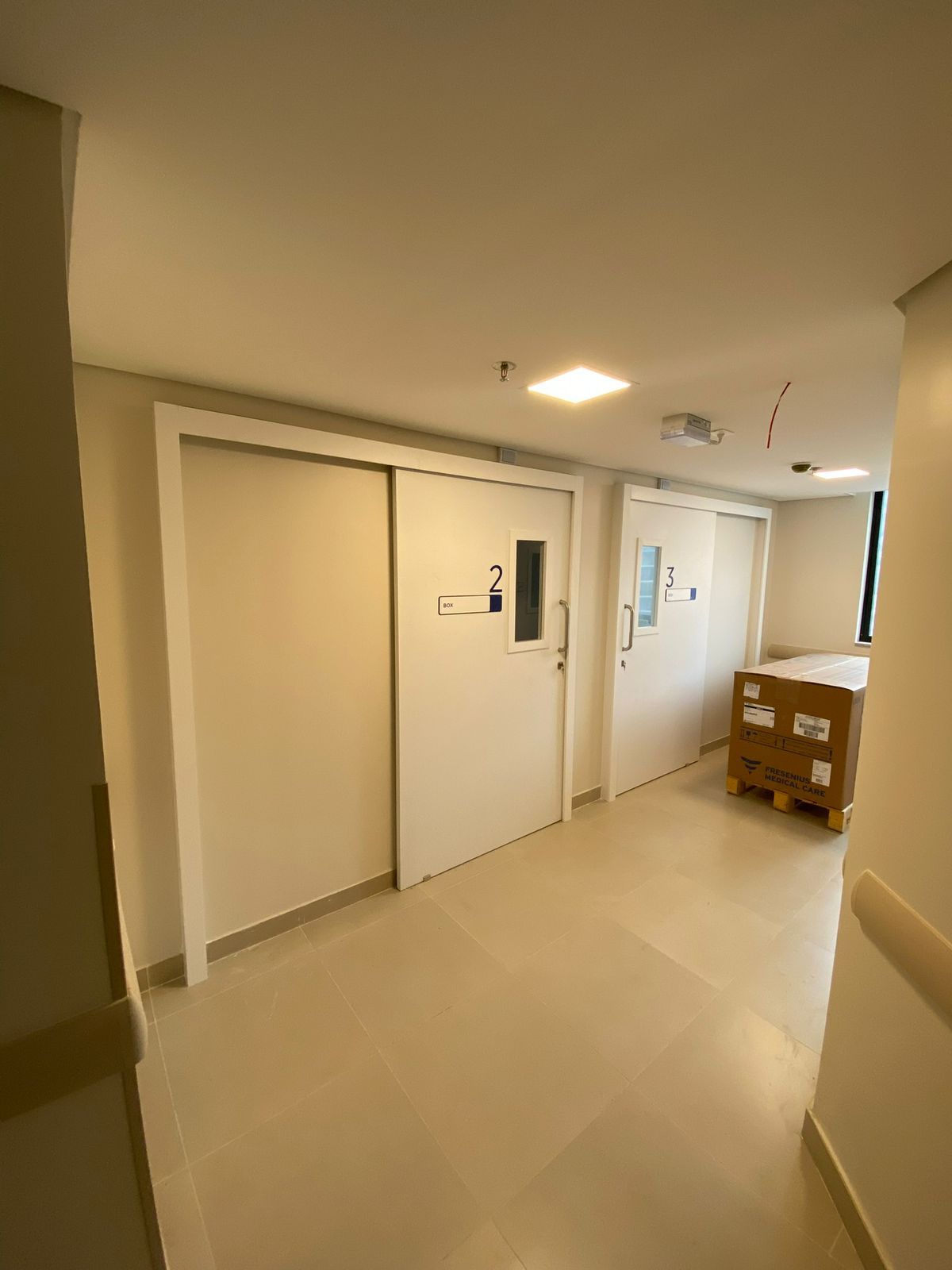 Um corredor de hospital com portas de correr e uma caixa no chão.