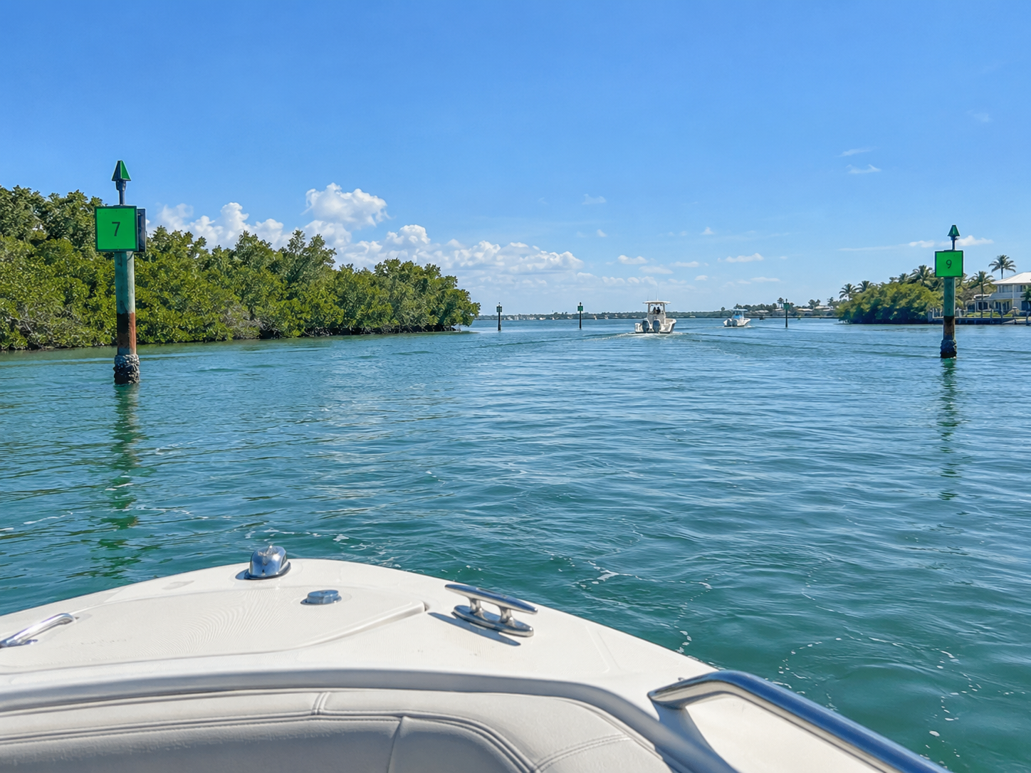 photographic view from a small rental boat looking down a marked Intracoastal Waterway channel near Anna Maria Island with green dayboards, calm water, and distant mangroves under clear sky