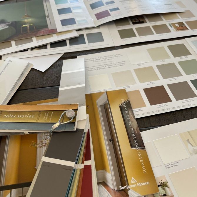 A top-down view of various Benjamin Moore paint color sample brochures, fan decks, and swatches on a flat surface.