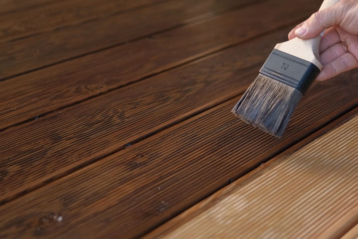 A person pours light green paint from a white bucket into a green roller tray on a drop cloth-covered floor.
