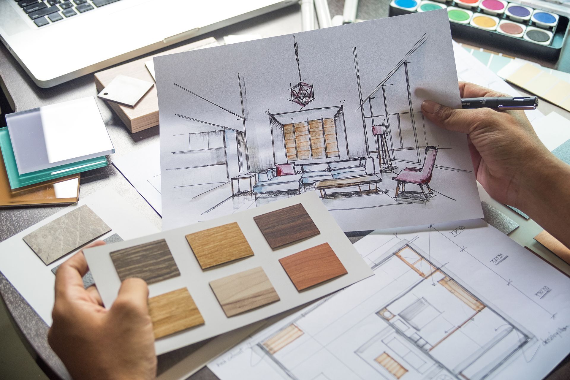 Hands holding interior design sketches and material swatches on a desk Hands holding interior design sketches and material swatches on a desk