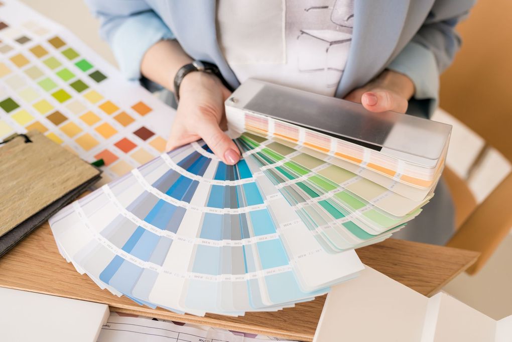 A person holds a fan of paint swatches in varying shades of blue and green, with a color palette on the table nearby.