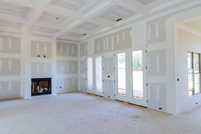 An unfinished room under construction with white drywall, a fireplace, coffered ceiling, and glass doors to the outside.