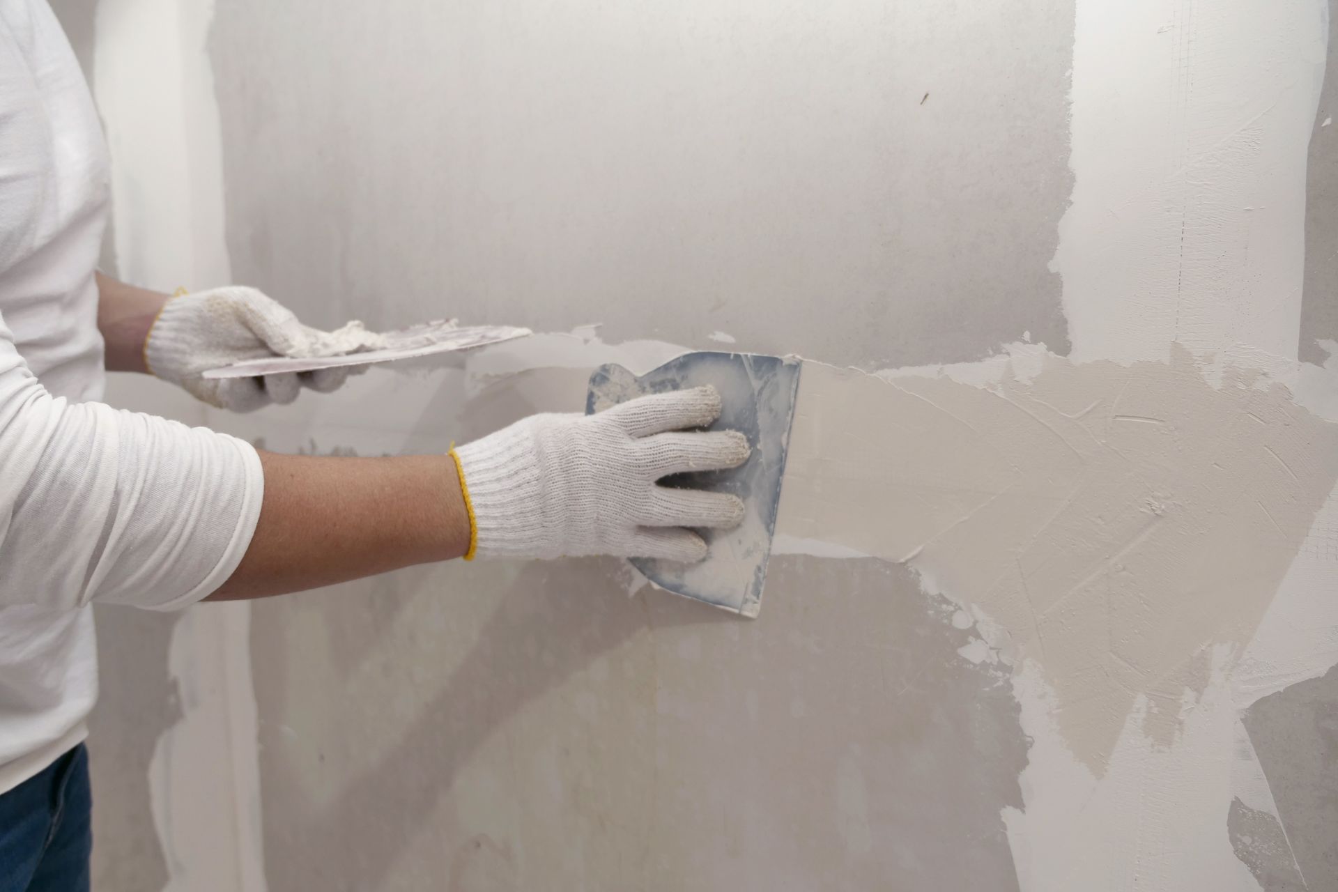 Person smoothing fresh plaster on a wall with a trowel and sanding block