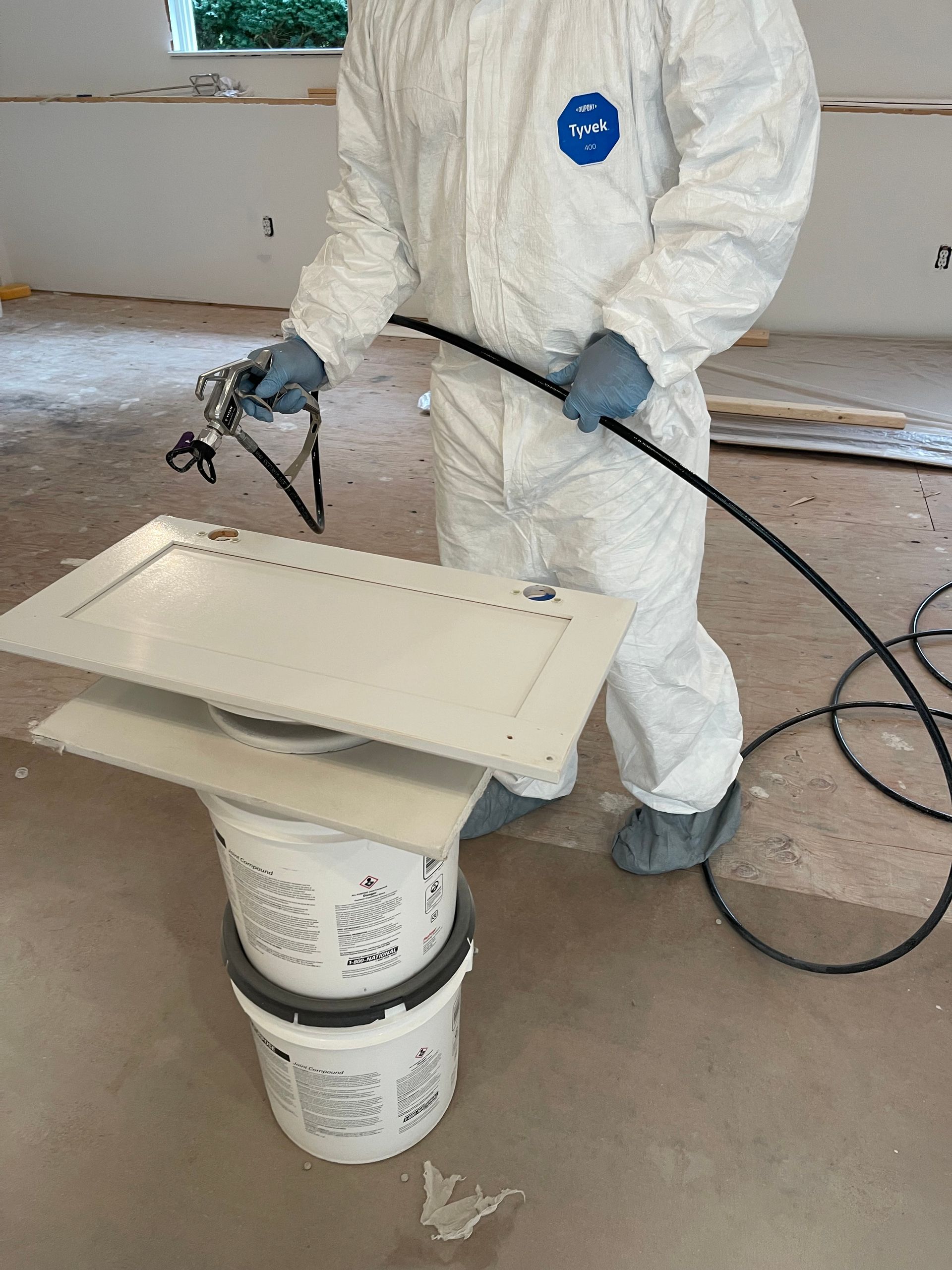 Worker in white protective suit spraying a beige object on a bucket stand with a hose.