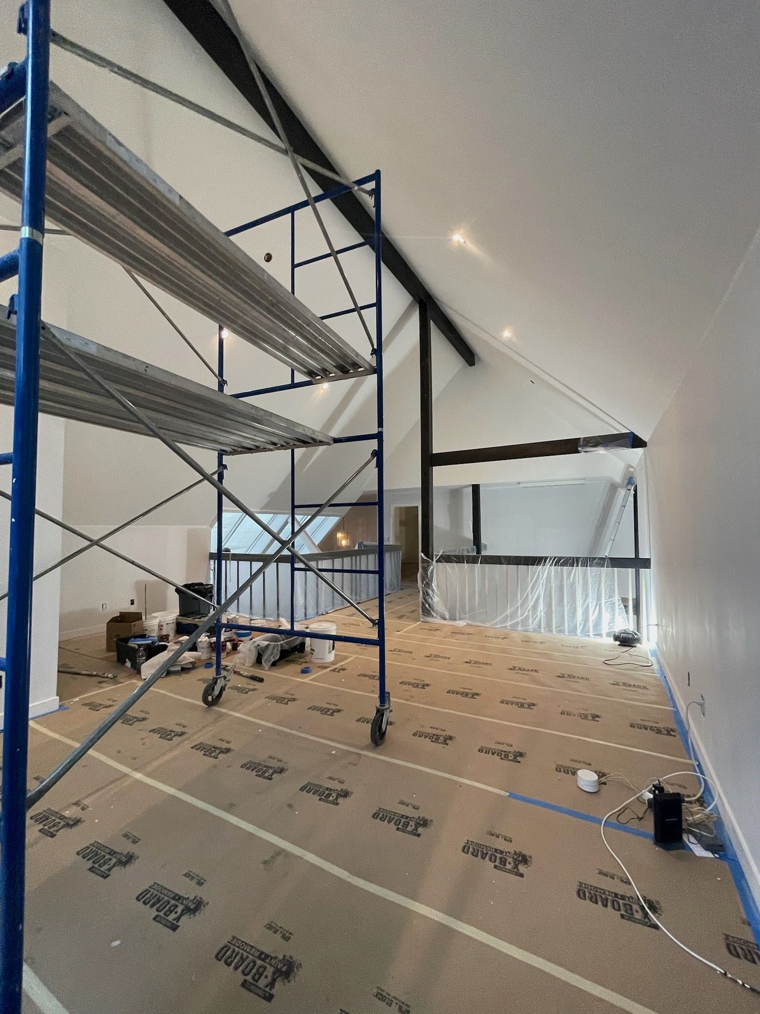 Unfinished room under renovation with coffered ceilings, construction tools, and a wooden ladder on a concrete floor.