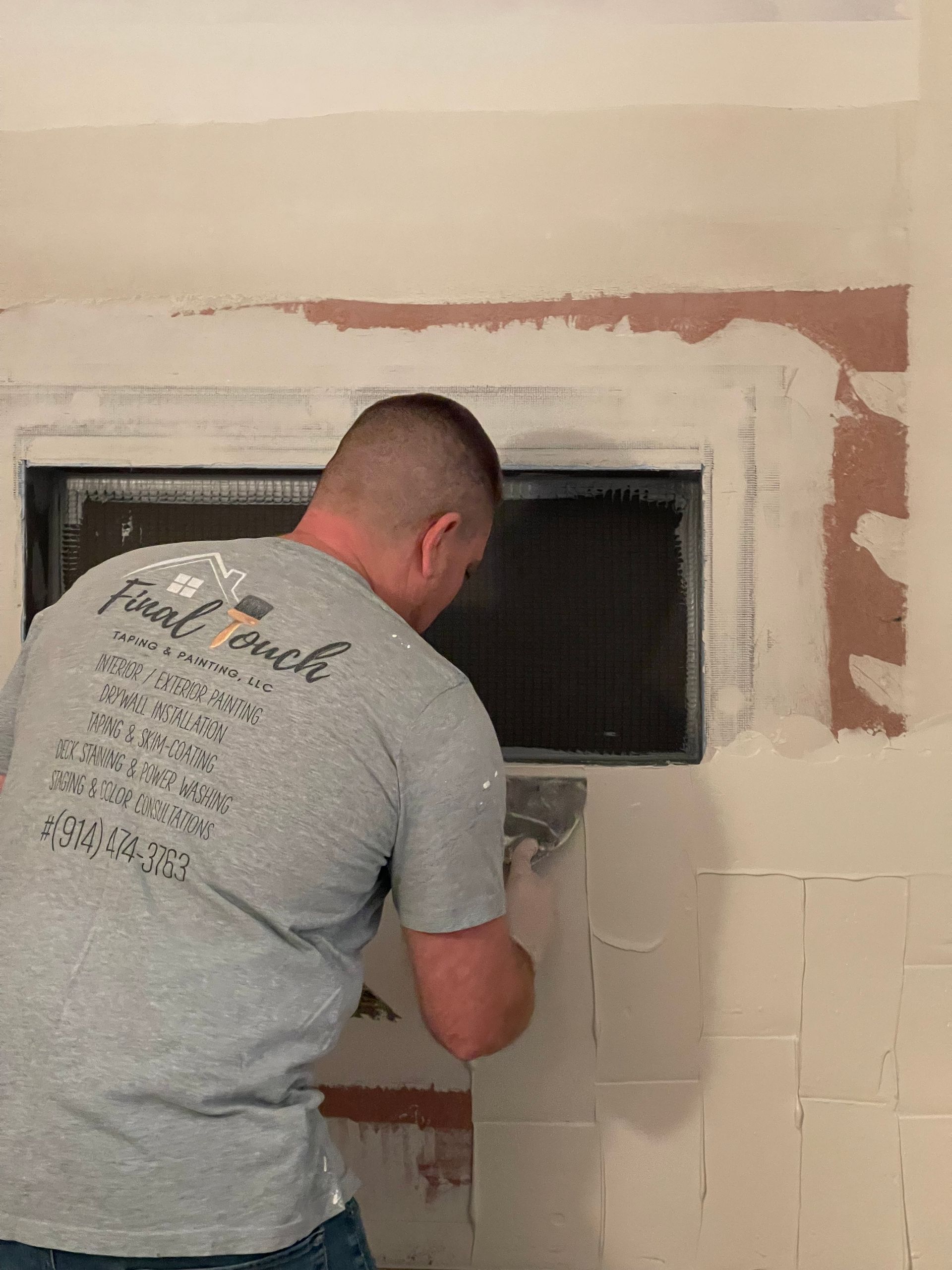 Worker installing a wall-mounted unit in a partially finished room with exposed drywall.