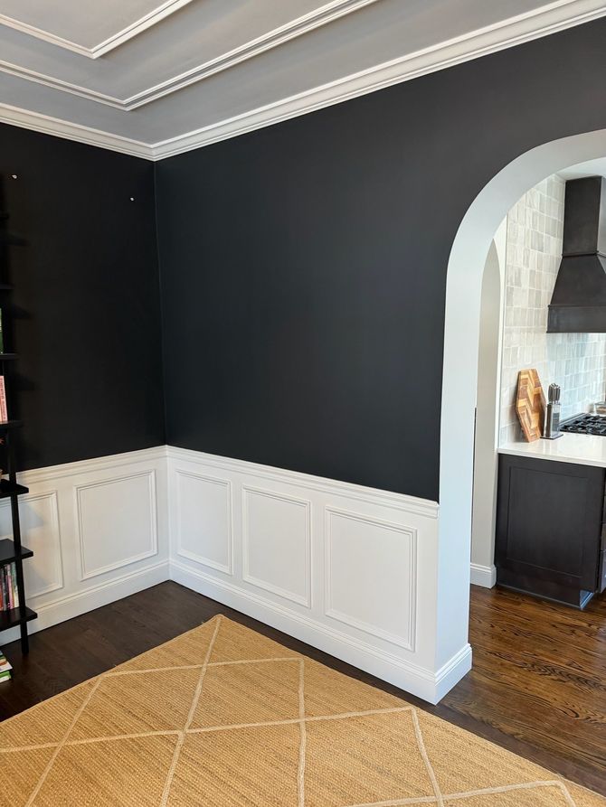 A multi-tiered iron chandelier hangs in a gray staircase landing featuring framed wall molding and a large window.