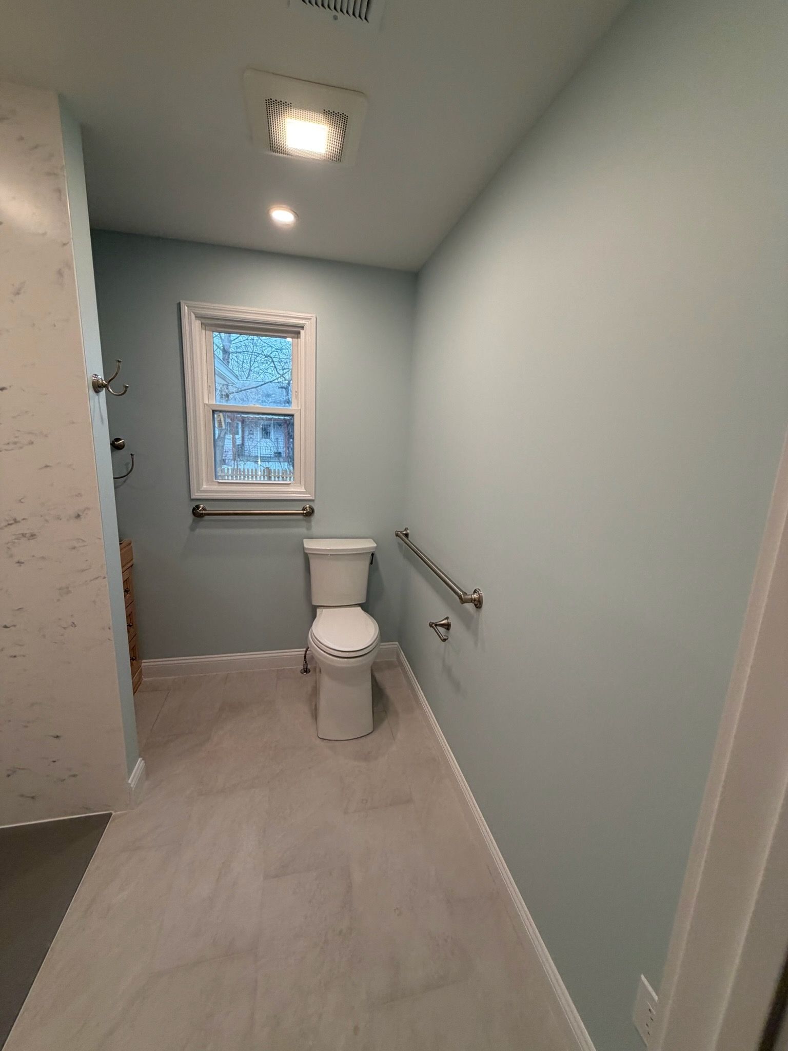 Small bathroom with white toilet, window, light blue walls, and tiled floor