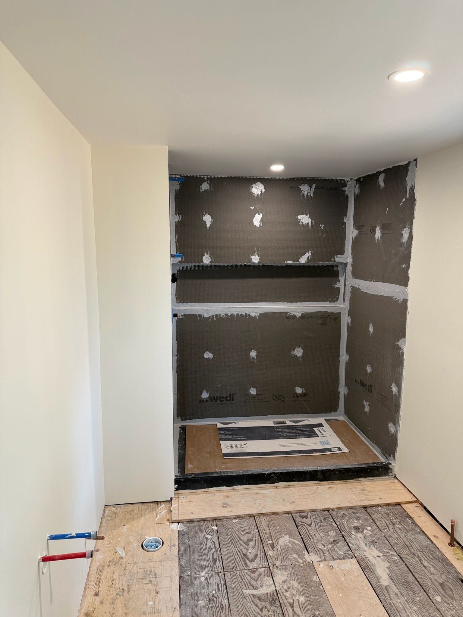 Small unfinished kitchen alcove with dark tile walls, white shelves, and construction materials on the floor