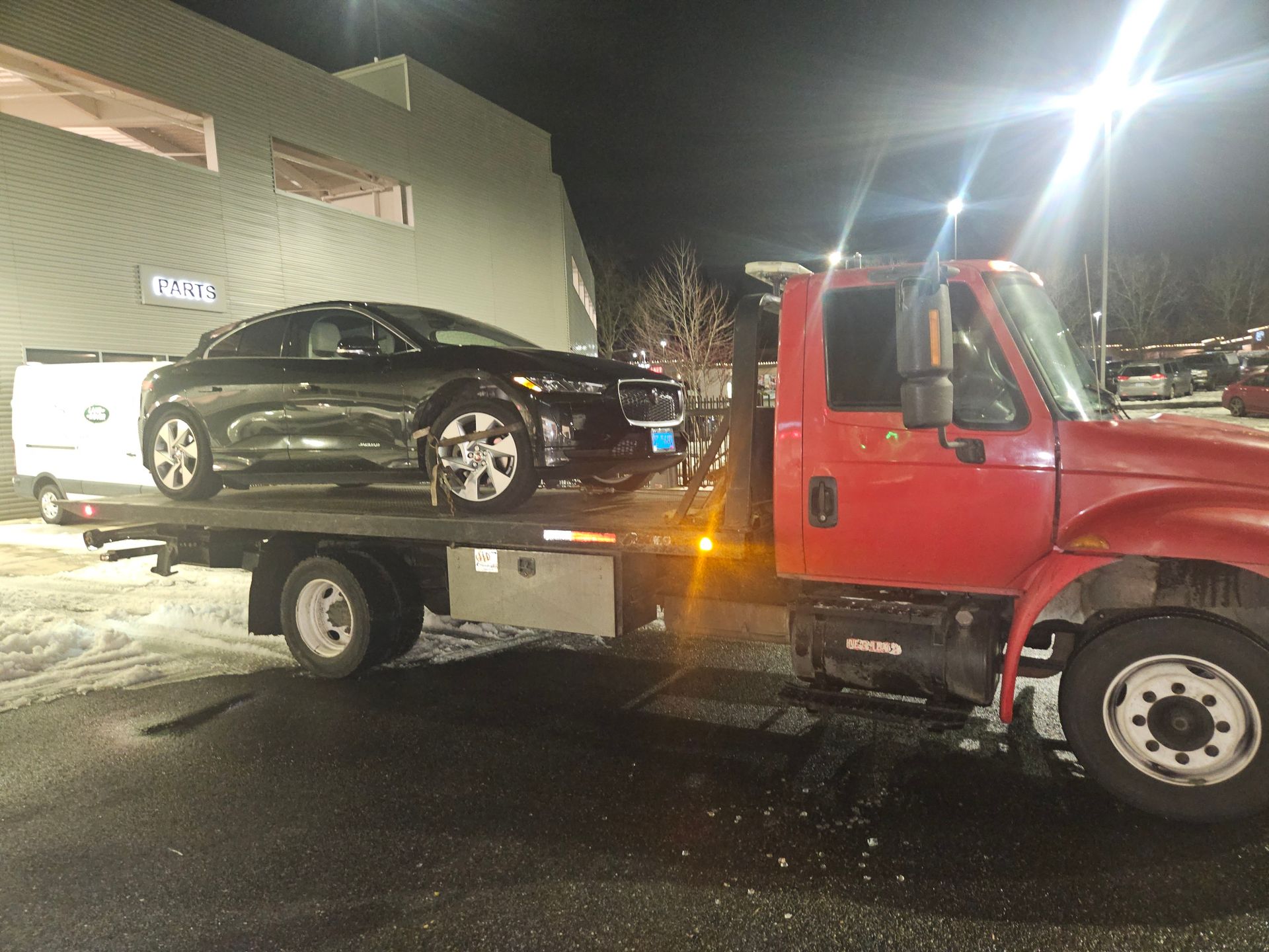 A red tow truck is carrying a black car on its back.