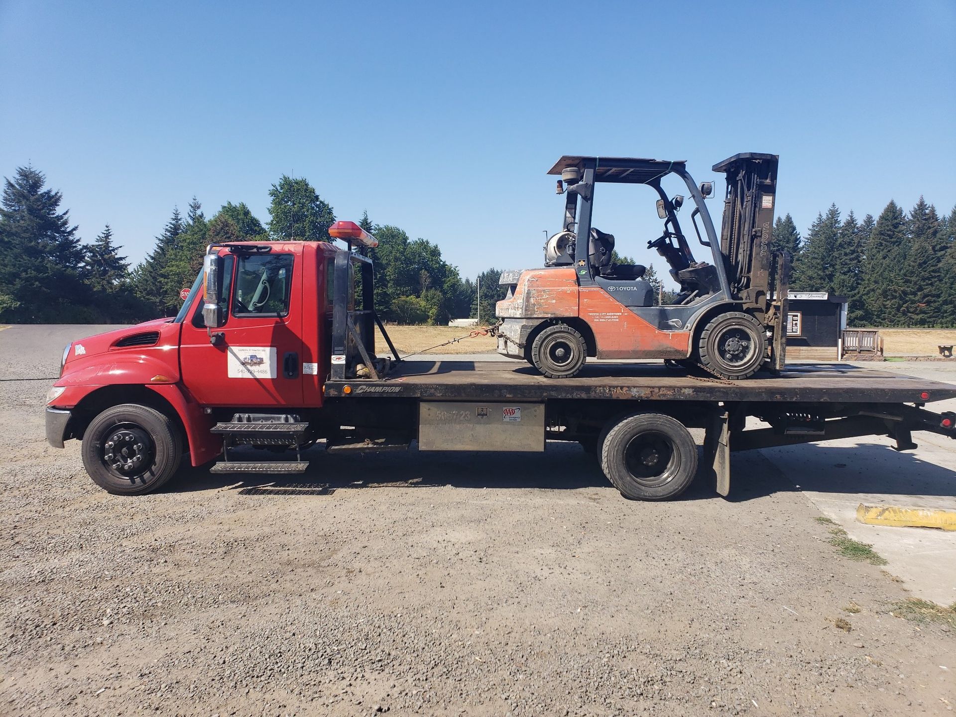 A red tow truck with a forklift on the back of it