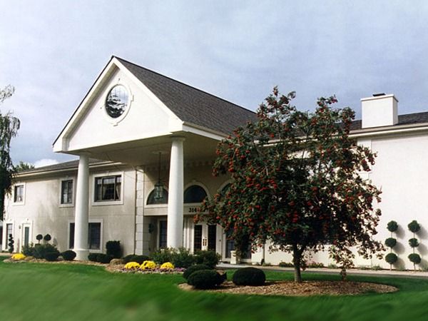 Large white colonial-style house with columns, a manicured lawn, and a flowering tree in front