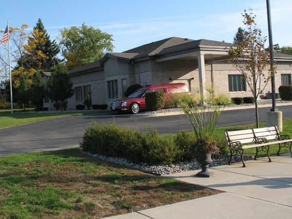 Building entrance with a red car, landscaped lawn, and a bench beside a sidewalk