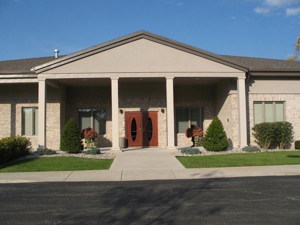 Suburban house entrance with columns, red double doors, and a front walkway under a clear blue sky