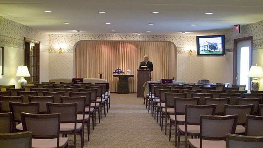 Empty conference room with rows of chairs facing a podium and speaker’s table at the front.