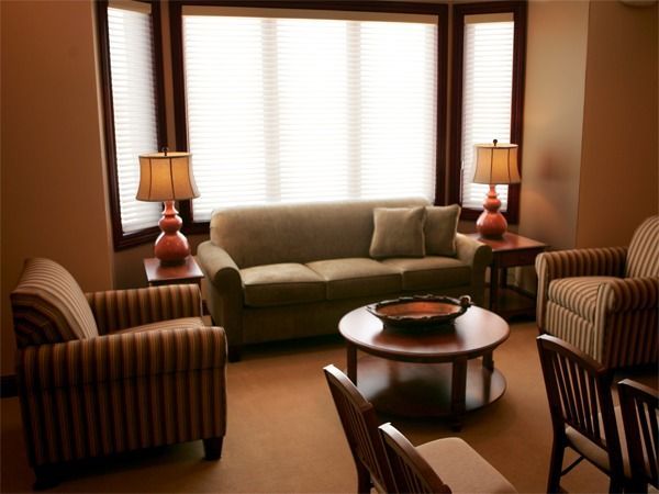 Cozy living room with green sofa, striped armchairs, round coffee table, and table lamps by a bright window