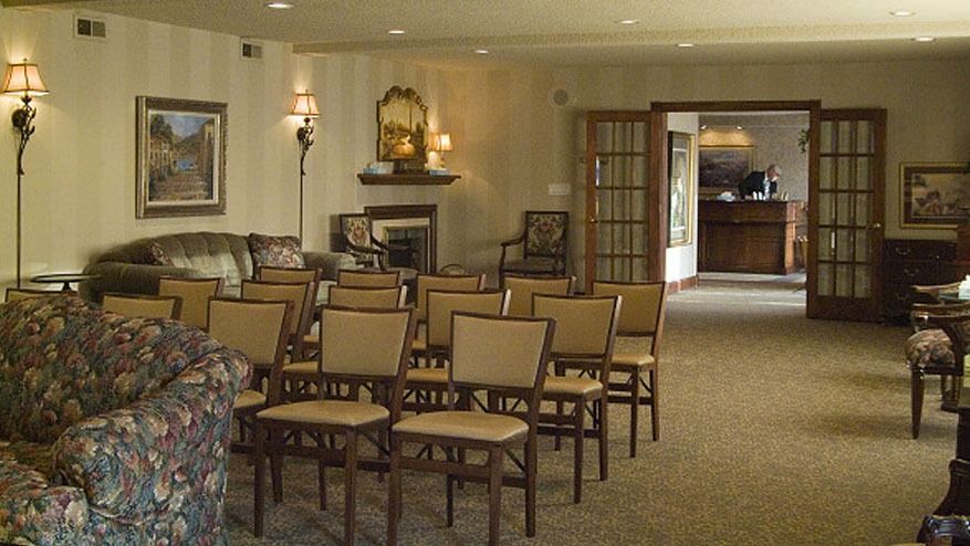 Empty hotel lounge with rows of chairs, patterned sofa, fireplace, and soft lighting