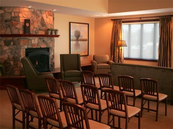 Empty meeting room with rows of wooden chairs, fireplace, framed art, and a window with curtains