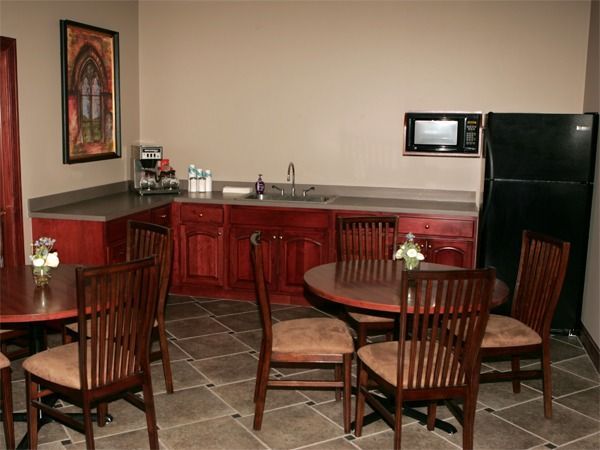 Small kitchenette with red cabinets, sink, black fridge, and two round wooden tables with chairs.