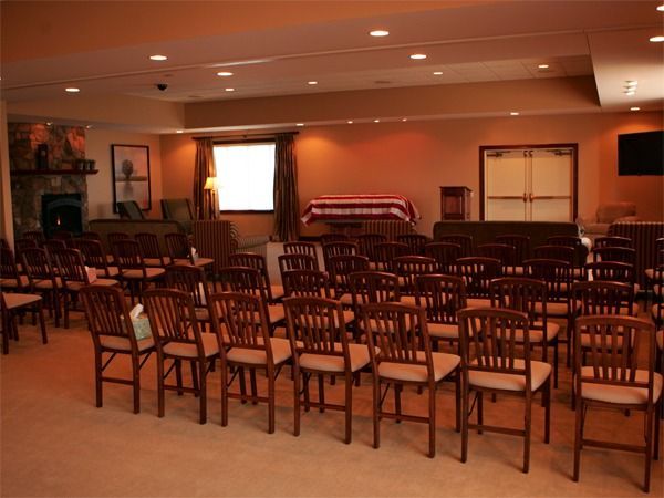 Empty banquet hall with rows of wooden chairs facing a stage and projector screen