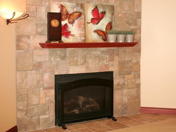 Stone fireplace with red mantel shelf, butterfly wall art, and decorative vases in a living room.