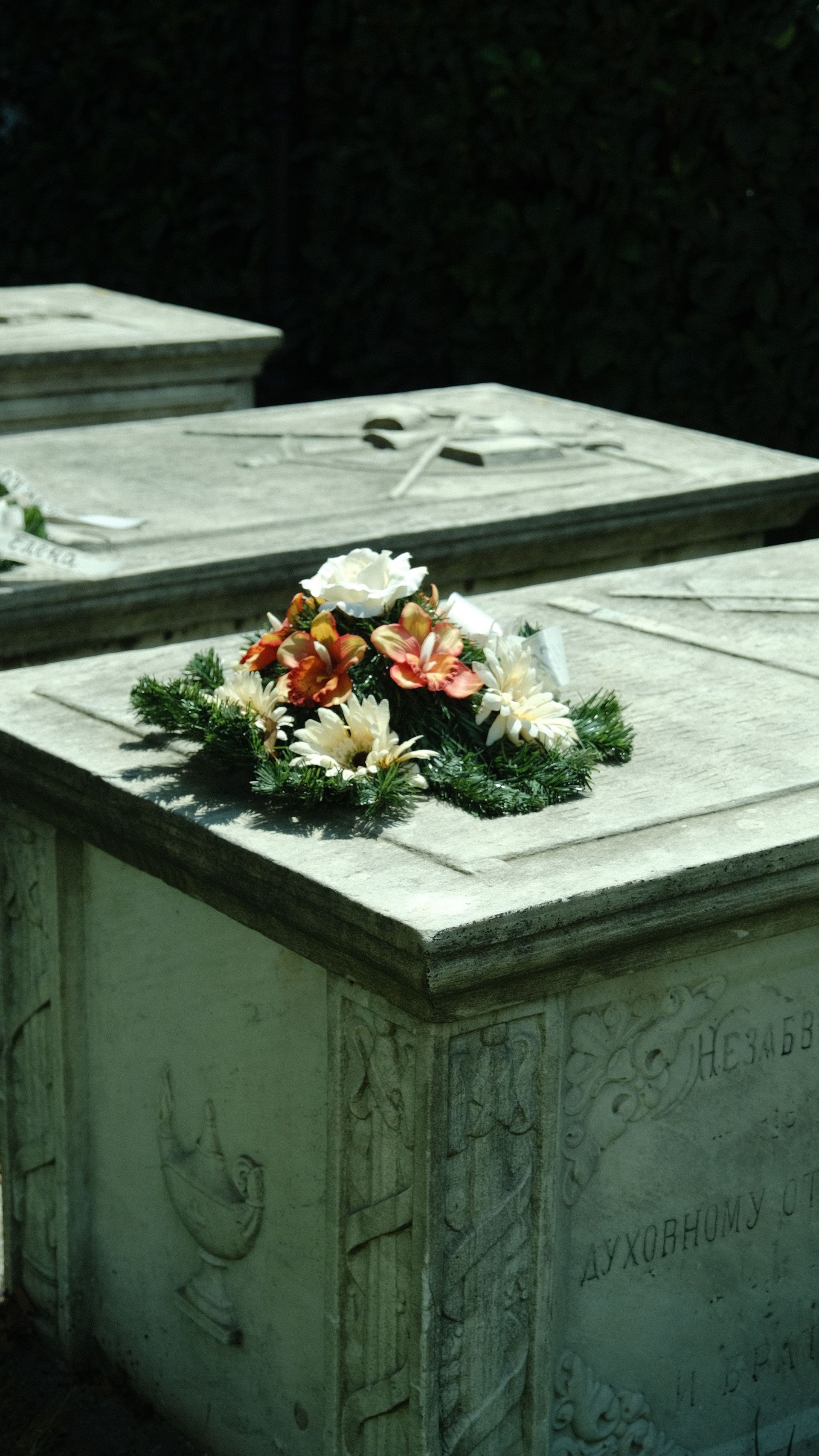 Flowers on a gray tombstone in a cemetery, with another tomb in the background.