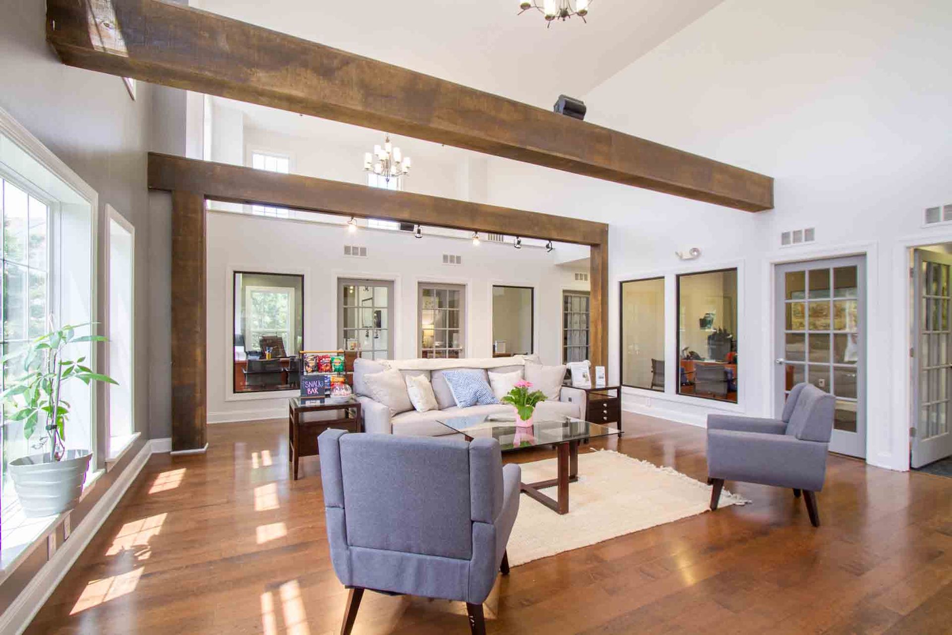 Lounge area with light gray walls, hardwood floor, two blue armchairs, sofa, coffee table, and large wooden beams at Hamburg Farms, offers apartments in Lexington, KY.