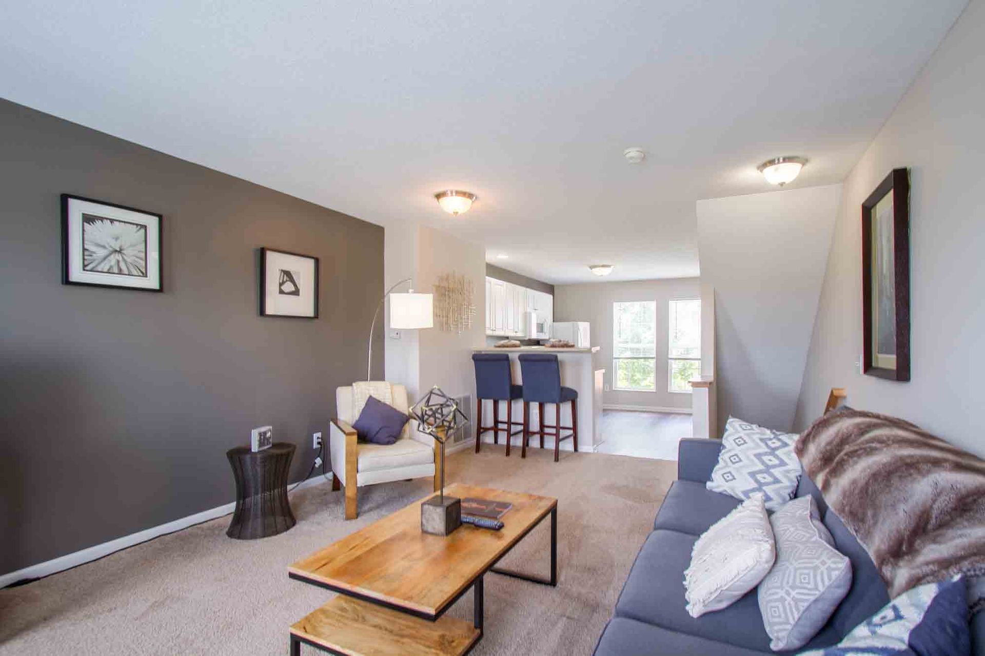 Living room with gray accent wall, sofa, armchair, coffee table, and open kitchen with bar stools at Hamburg Farms, offers Lexington apartments for rent.