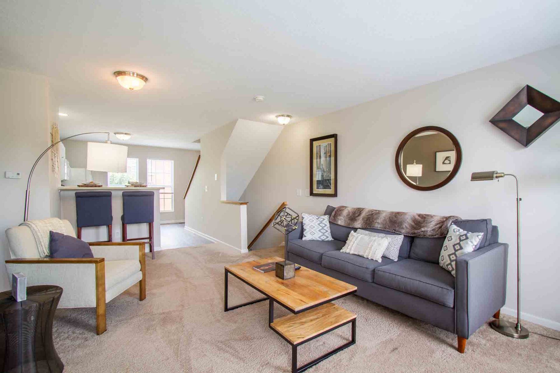 Living room with gray sofa, white armchair, coffee table, and stairs at Hamburg Farms, offers Lexington apartments for rent.