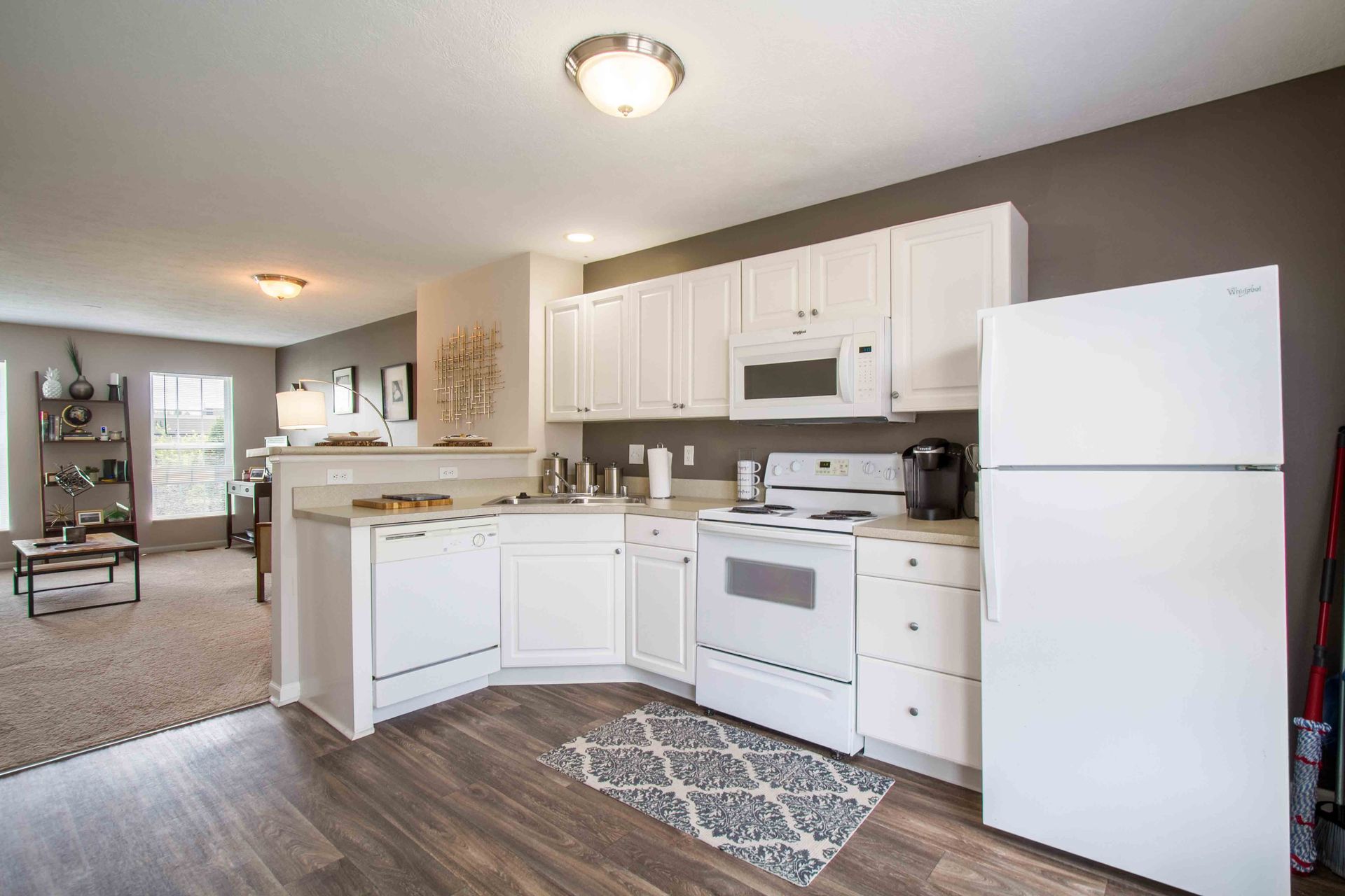 White kitchen with cabinets, appliances, and gray wall at Hamburg Farms, offers Lexington apartments for rent. Wood-look floor. Leads to living room.