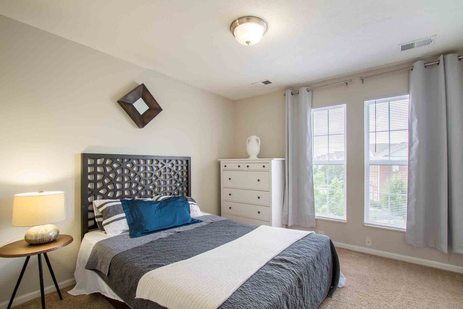 Bedroom with bed, dresser, table lamp, and two windows with sheer curtains at Hamburg Farms, offers Lexington apartments for rent.