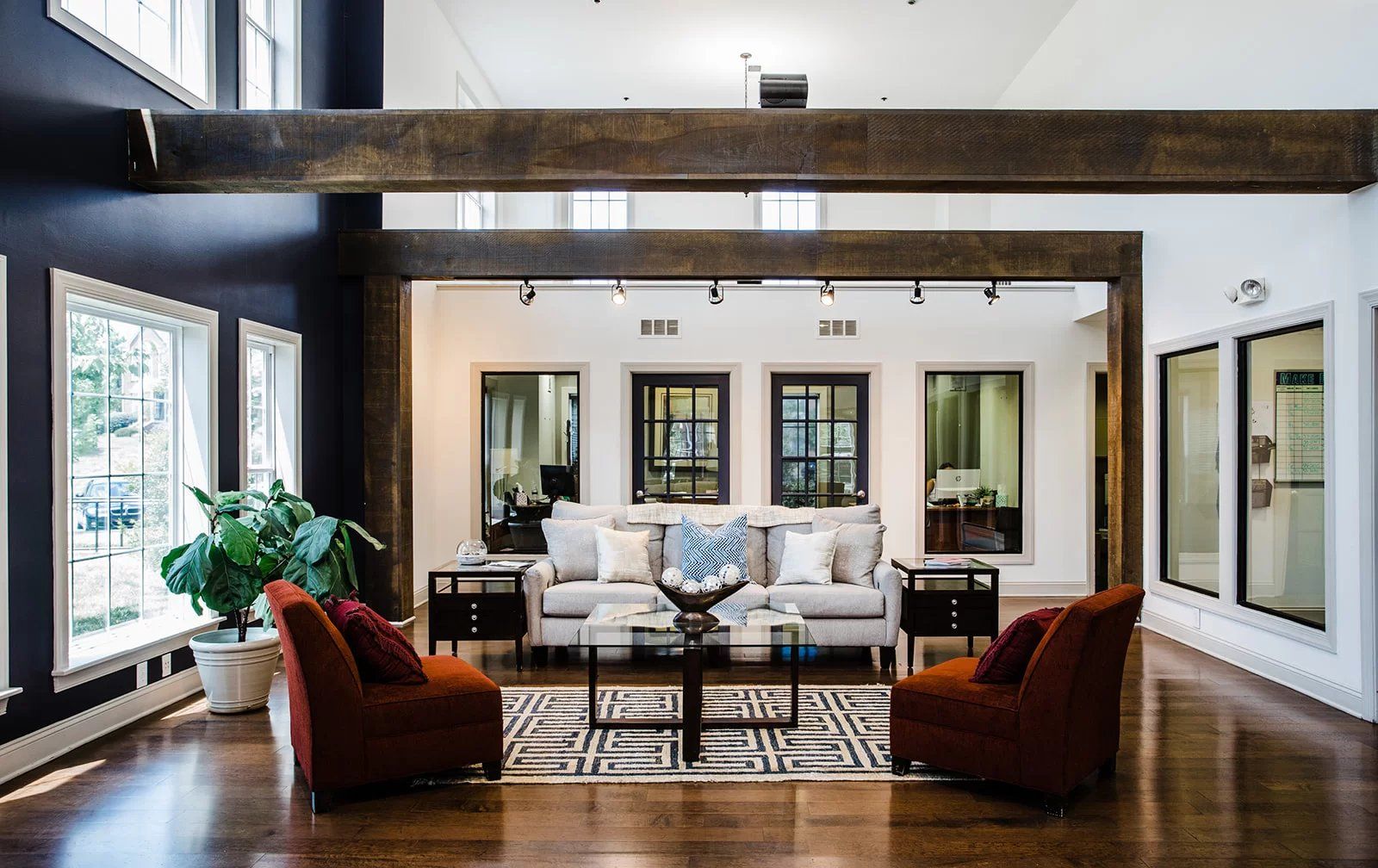 Lobby with two red armchairs, sofa, coffee table, and dark wood accents. Large windows and hardwood floors.