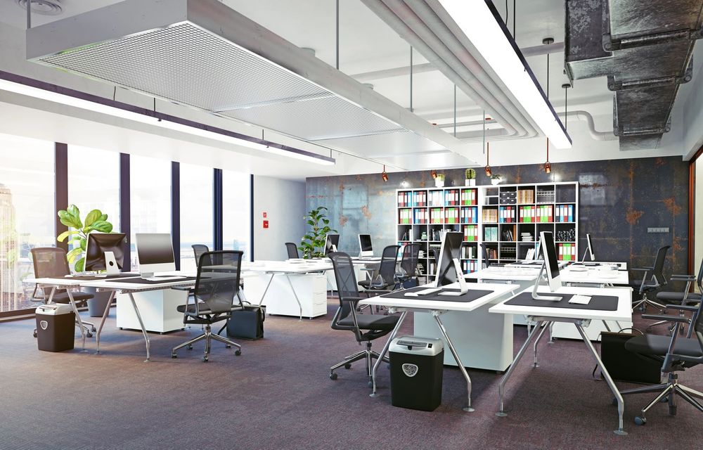 Moderno ufficio open space con scrivanie, sedie, librerie e ampie finestre che creano un ambiente di lavoro luminoso