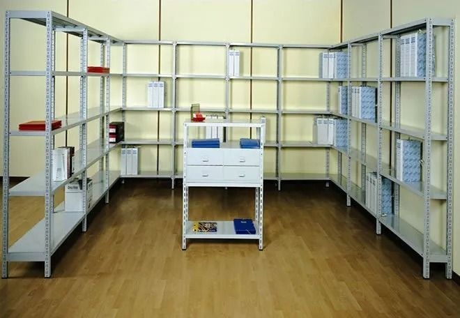 Scaffalature metalliche vuote in un ripostiglio con pavimento in legno e un piccolo carrello bianco al centro