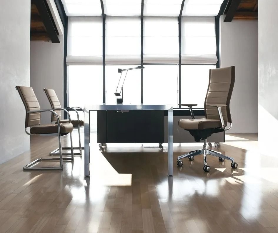 Ufficio moderno con una scrivania in vetro, due sedie beige e la luce del sole che filtra dalle grandi finestre