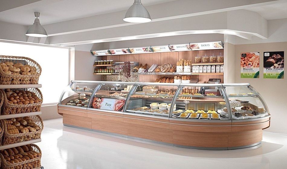 Panetteria luminosa con vetrine per i dolci e scaffali di pane, illuminata da lampade a sospensione